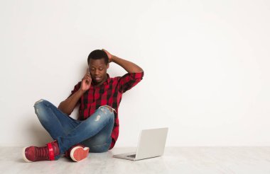 Telefon kullanan siyah adam ve stüdyo katta oturan dizüstü düşünme