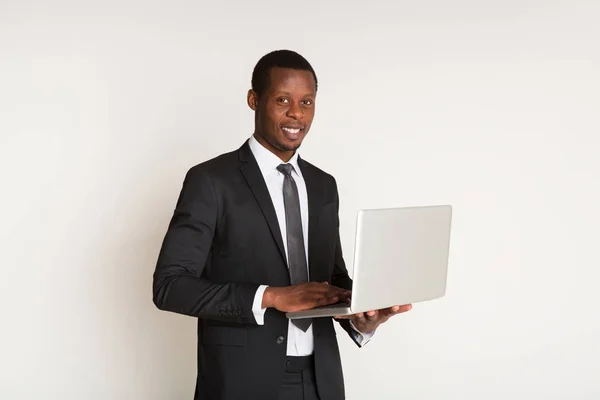 Hombre negro feliz gerente en traje, corbata de pie, sosteniendo el ordenador portátil en las manos. Retrato — Foto de Stock