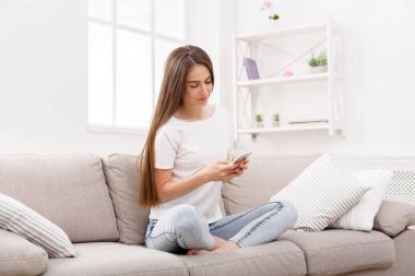 Smartphone evde kanepede kullanan genç kadın. Casual manifatura online esmer kız