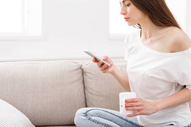 Smartphone evde kanepede kullanan genç kadın. Casual manifatura online esmer kız