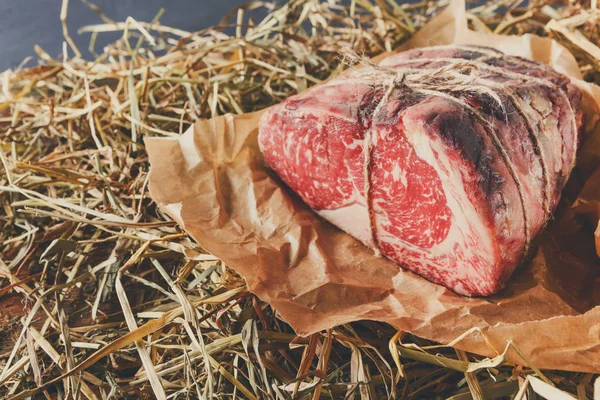 Raw aged prime black angus beef in craft papper on straw — Stock Photo, Image