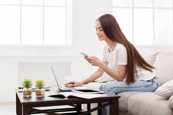 Bella ragazza che messaggia sul cellulare a casa sul divano. Ragazza dai capelli scuri in casual — Foto Stock