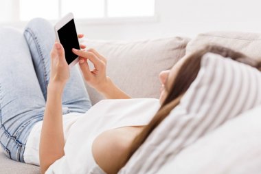 Smartphone evde kanepede kullanan genç kadın. Casual manifatura online esmer kız