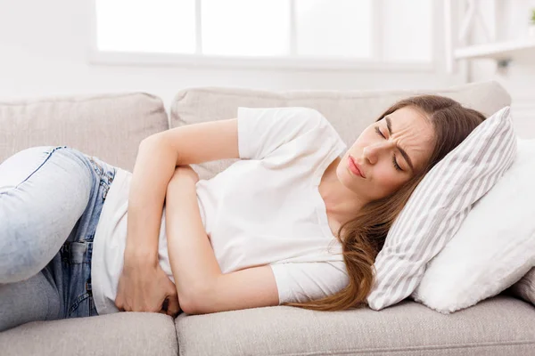 Chica joven que sufre de dolor de estómago acostado en el sofá — Foto de Stock