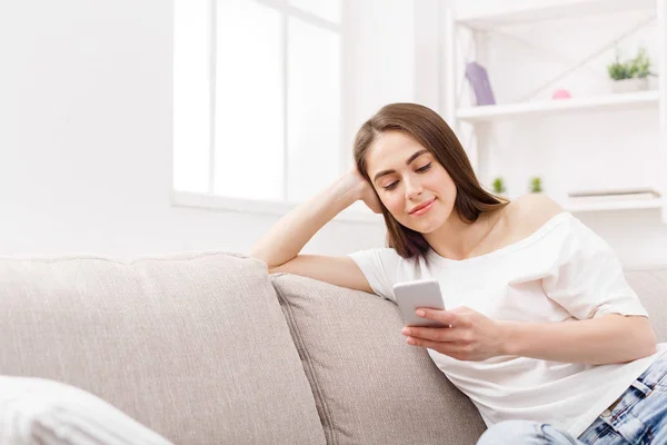 Jovem mulher usando smartphone em casa no sofá. Menina de cabelos escuros em mensagens de texto casual online — Fotografia de Stock