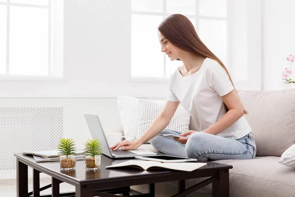 Hübsches Mädchen, das zu Hause auf der Couch auf dem Laptop tippt. dunkelhaarige Mädchen in lässig — Stockfoto