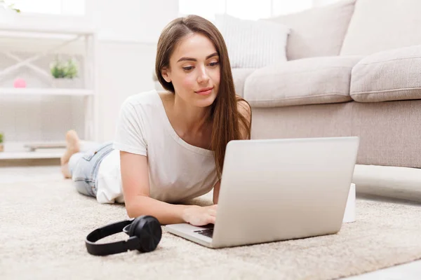 Šťastná dívka online chatování na notebooku, ležící na podlaze koberec — Stock fotografie