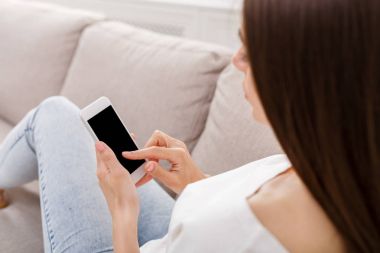 Smartphone evde kanepede kullanan genç kadın. Casual manifatura online esmer kız