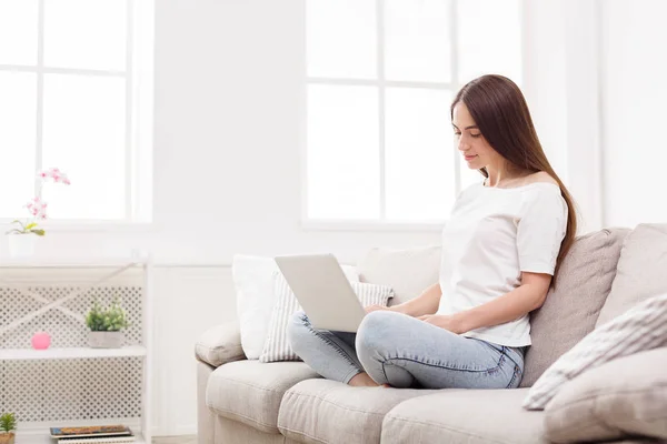 Young women using laptop sitting on sofa in white livingroom — Stock Photo, Image