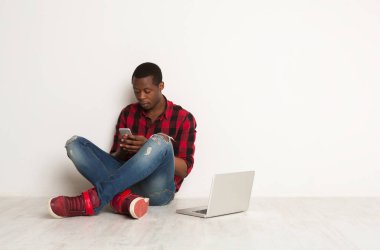 Düşünceli siyah adam akıllı telefon, laptop studio katta oturan yazarak