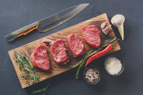 Filet mignon steaks en specerijen op hout op zwarte achtergrond — Stockfoto
