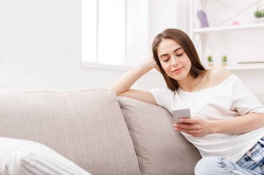 Smartphone evde kanepede kullanan genç esmer kadın. Casual manifatura online esmer kız