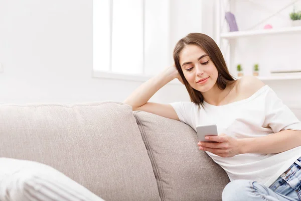 Fiatal barna nő használ smartphone otthon a kanapén. Sötét hajú lány alkalmi textil-online — Stock Fotó