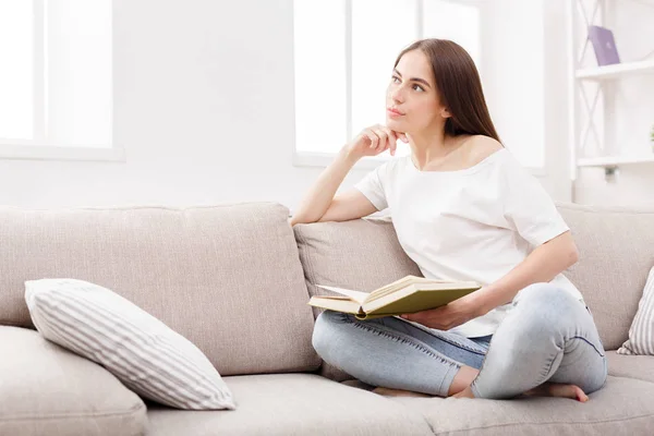 若いブルネットの女性自宅ソファで本を読んで. — ストック写真