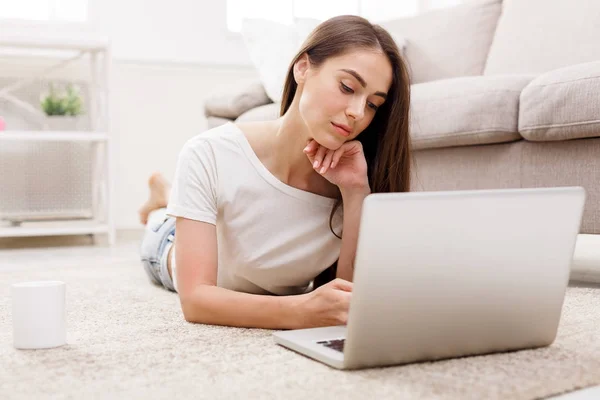 Junge Frauen chatten online auf dem Laptop, während sie auf dem Teppich liegen — Stockfoto