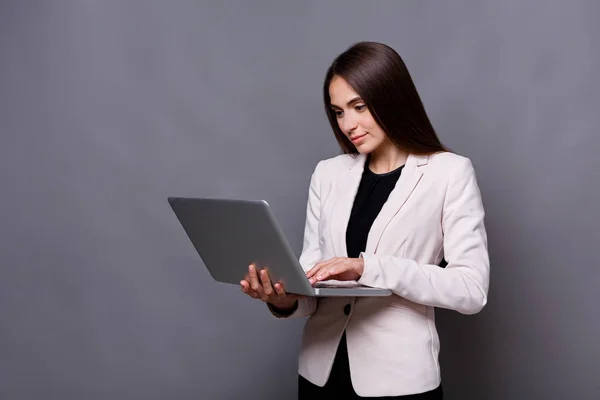 Koncentrovaných obchodních žena s laptopem na šedém pozadí — Stock fotografie
