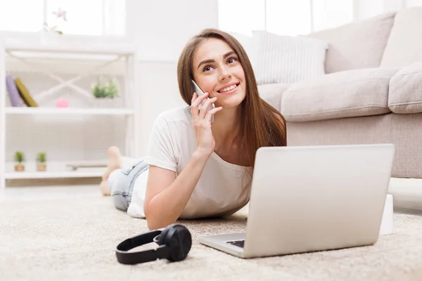 Giovani donne che parlano sul cellulare chattando online sul computer portatile mentre si trovano sul tappeto pavimento — Foto Stock