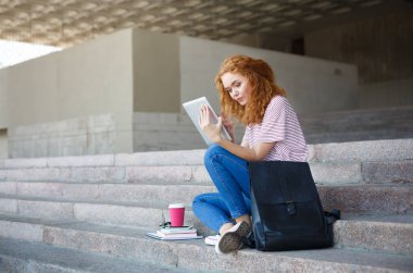 Genç Kızıl saçlı kız öğrenci tablet, merdivenlerde açık havada oturma ile çalışma