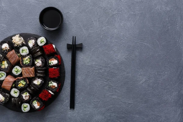 Σετ από μαύρες σούσι κυλίνδρους, maki με chopsticks σε γκρίζο φόντο, το top view — Φωτογραφία Αρχείου