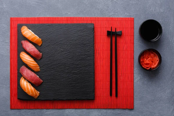 Sushi set a hůlky na červený mat na šedém pozadí, pohled shora — Stock fotografie