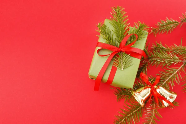 Συσκευασία δώρου στο χαρτί περιτυλίγματος πράσινο, Χριστούγεννα καμπάνες, πεύκο σε κόκκινο φόντο. Χώρο αντίγραφο — Φωτογραφία Αρχείου