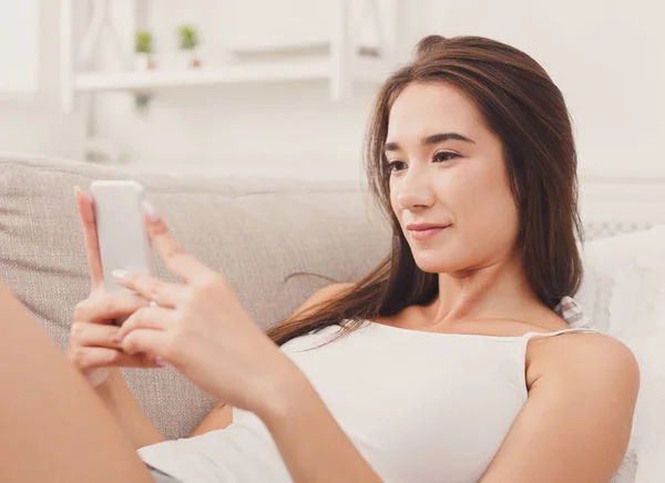 Chica joven usando el teléfono móvil en el sofá — Foto de Stock