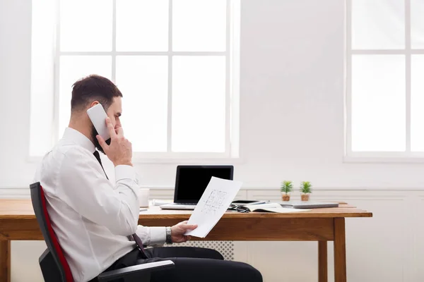 Ernstige zakenman praten op mobiele telefoon met laptop in moderne kantoren — Stockfoto