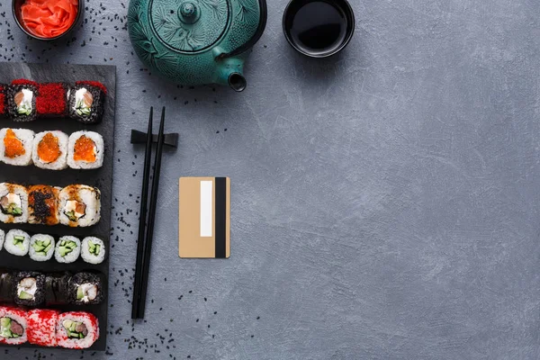 Üstten Görünüm suşi maki ve çaydanlık ve kredi kartı ile rulo rustik gri ve susam arka plan üzerinde kümesi — Stok fotoğraf