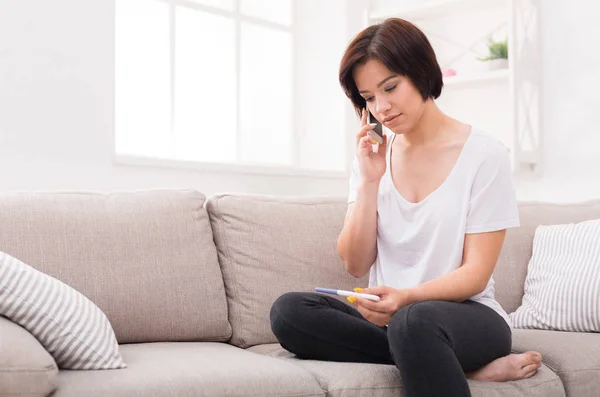 Upset girl holding pregnancy test and making call — Stock Photo, Image