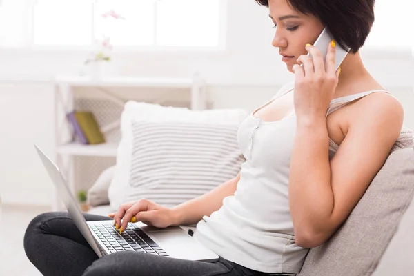 Pensive girl with laptop and mobile sitting on beige couch — Stock Photo, Image