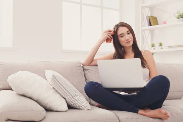 Chica joven con el ordenador portátil sentado en el sofá beige — Foto de Stock