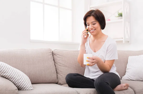 Lachende meisje thuis praten op smartphone en koffie drinken — Stockfoto