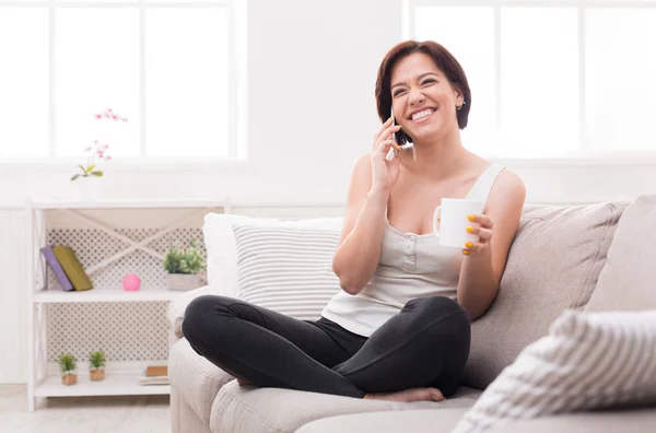 Молодая возбужденная женщина разговаривает по телефону и пьет кофе — стоковое фото
