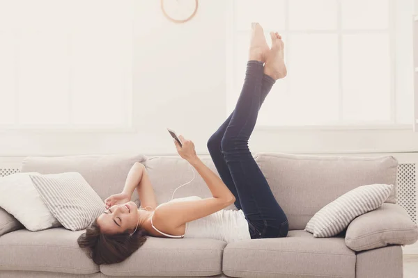 Gelukkig jonge vrouw in de koptelefoon op beige couch — Stockfoto