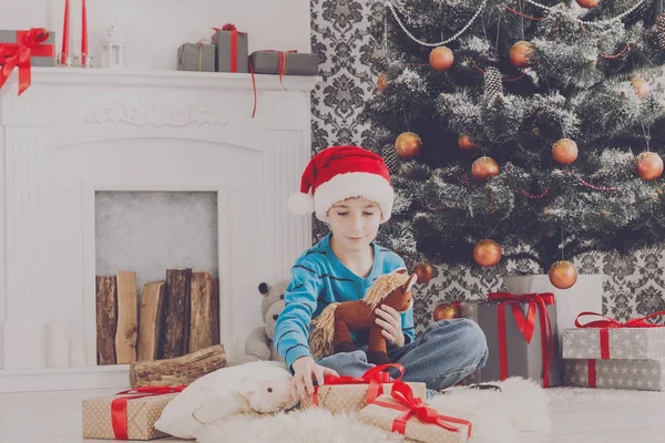 Carino ragazzo felice in cappello di Babbo Natale con giocattoli regali di Natale — Foto Stock