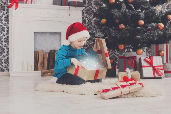 Bonito menino feliz em santa chapéu desembrulhando presentes de Natal — Fotografia de Stock