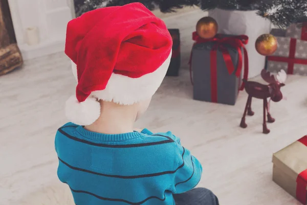 Menino bonito em santa chapéu desembrulhando presentes de Natal — Fotografia de Stock