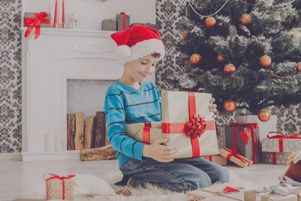 Menino bonito em santa chapéu desembrulhando presentes de Natal — Fotografia de Stock