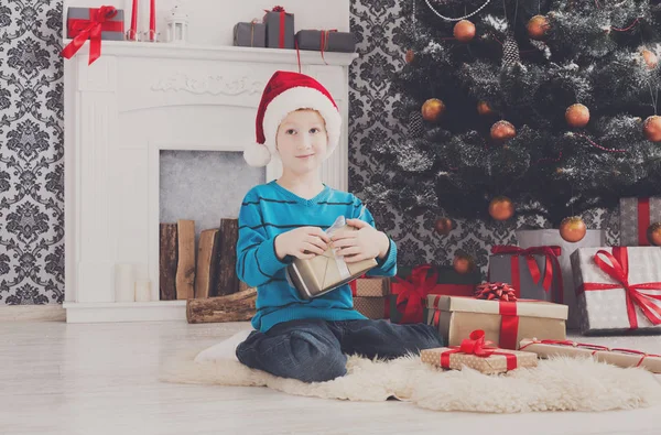 Süßer Junge mit Weihnachtsmütze beim Auspacken von Weihnachtsgeschenken — Stockfoto