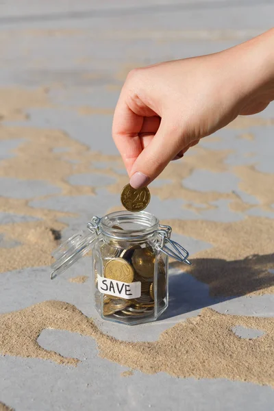 Рука кладе монети в скляну банку з етикеткою SAVE — стокове фото