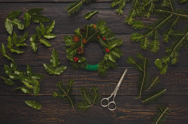 Corona de Navidad hecha a mano. Abeto, hojas, tijeras sobre fondo rústico — Foto de Stock