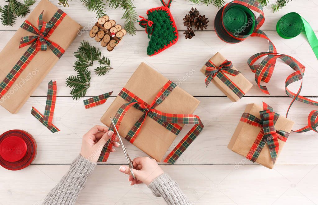 Female hands packaging xmas gifts at messy table background