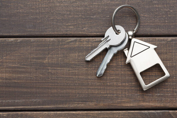 Куча ключей с брелоком в форме дома на коричневом дереве
