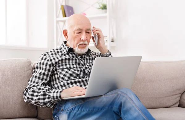 ノート パソコンと携帯電話で話している年配の男性 — ストック写真