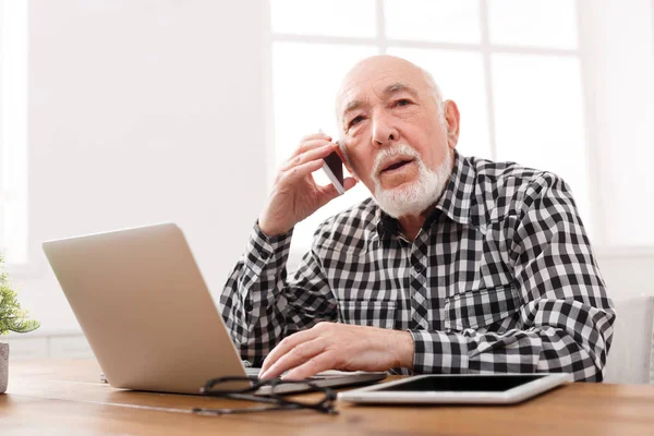 Senior man talking on phone with laptop