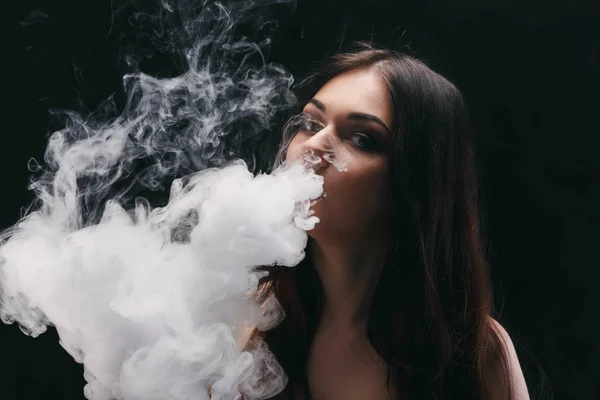 Mujer joven vapeando e-cigarrillo con humo en negro — Foto de Stock