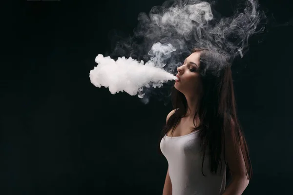 Mujer joven vapeando e-cigarrillo con humo en negro — Foto de Stock