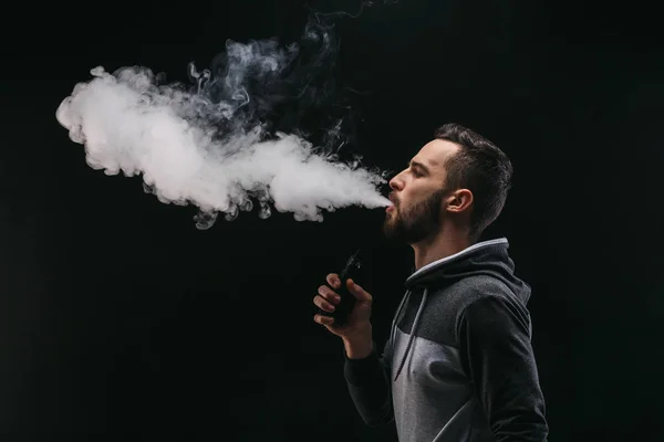 Homem jovem vaping e-cigarro com fumaça em preto — Fotografia de Stock