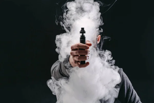 Hombre joven vapeando e-cigarrillo con humo en negro — Foto de Stock