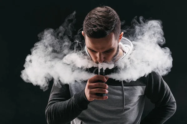 Junger Mann verdampft E-Zigarette mit Rauch auf schwarz — Stockfoto